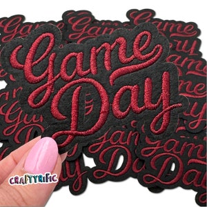 May include: A pile of black felt patches with red embroidered text that reads "Game Day".