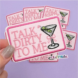 May include: Pink embroidered patch with the text "TALK DIRTY TO ME" and a martini glass with olives. The patch has a pink border and is surrounded by other similar patches.