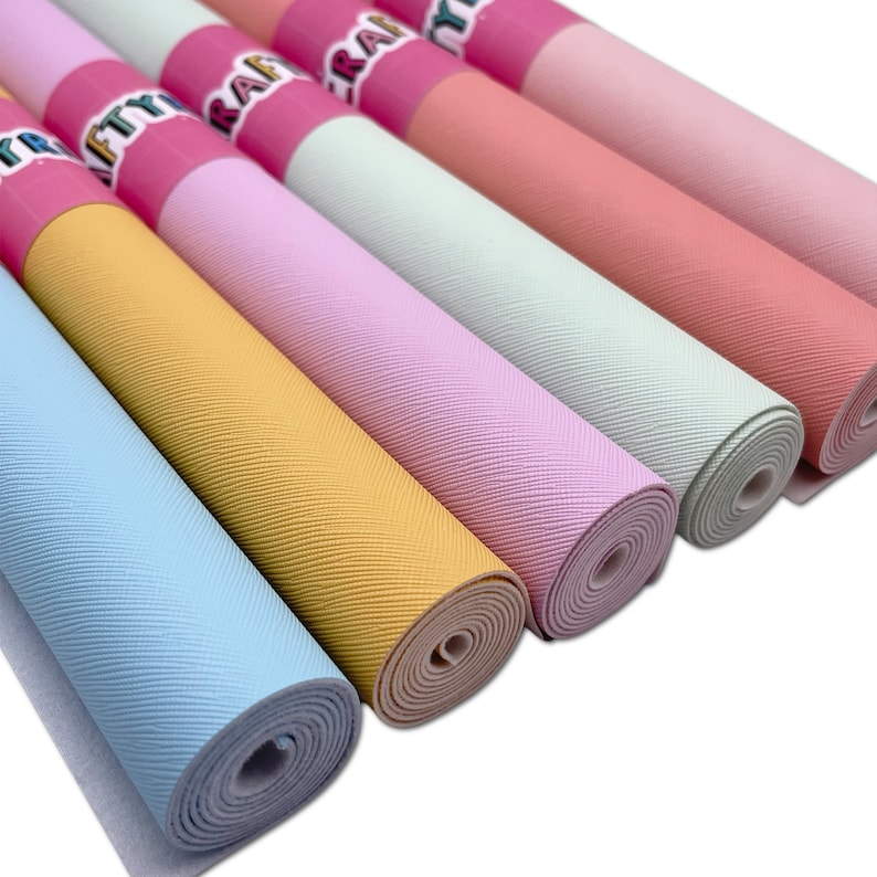 May include: A collection of rolled-up craft paper in various pastel colors, including blue, yellow, pink, and green. Each roll has a textured surface and is labeled with pink and white branding.