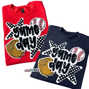 May include: Two sweatshirts with a black and white checkered starburst design with the words "game day" in black and white. The starburst also includes a baseball and a brown and white baseball glove.