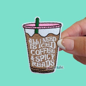 May include: An embroidered patch shaped like a plastic cup of iced coffee with a green straw and a pink lid. The brown coffee liquid features the white embroidered text: ALL I NEED IS ICED COFFEE & SPICY READS. The patch has a white border.
