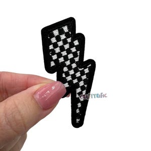 May include: Black and white checkered lightning bolt iron-on patch. The patch is made of fabric and has a black outline.