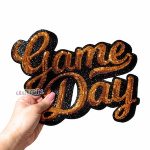 May include: Gold sequined iron-on patch with the words "Game Day" in a black background.