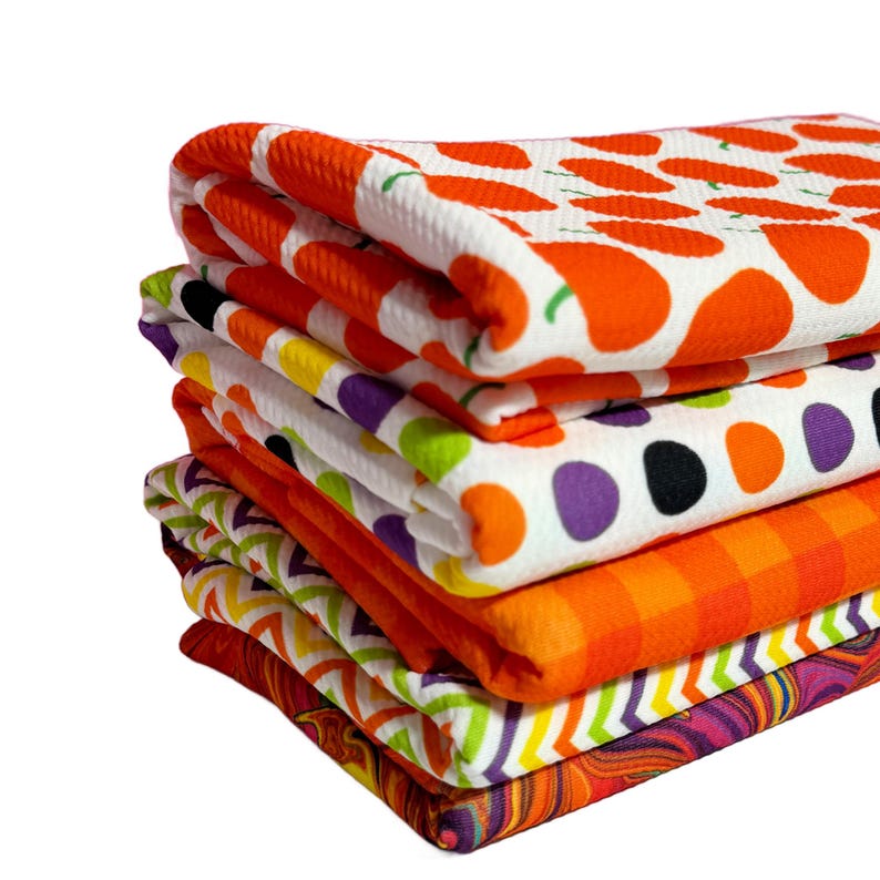 K&ouml;nnte beinhalten: Ein Stapel von sechs bunten K&uuml;chent&uuml;chern mit verschiedenen Mustern, darunter orange und wei&szlig;e Punkte, orange und wei&szlig;e geometrische Muster und ein lila und orangefarbenes Wirbelmuster.