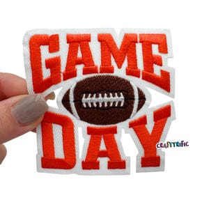 May include: Orange and brown embroidered iron-on patch with the text "GAME DAY" and a football in the center.