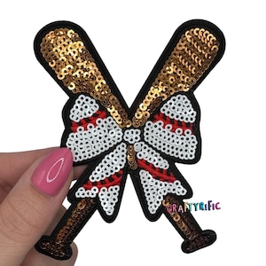 May include: A baseball-themed sequin patch featuring two crossed baseball bats with gold sequins. The center has a bow shape with white sequins and red stripes. The patch has a black border and the text "CraftyRific".