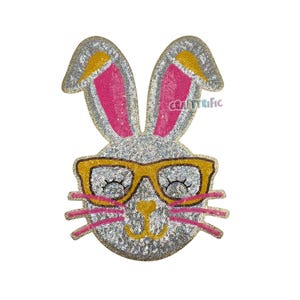 K&ouml;nnte beinhalten: Ein glitzernder silberner Hase mit rosa Ohren und gelben Brillen. Der Hase hat ein s&uuml;&szlig;es L&auml;cheln und ist aus Pailletten gefertigt.