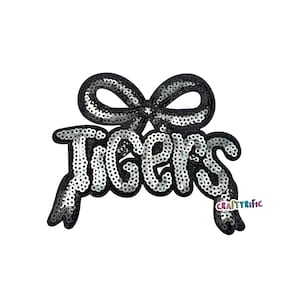 May include: A black and silver sequined patch with the word "Tigers" in a stylized font, topped with a bow. The patch has a black border and is on a white background. The text "CraftyRific" is in the lower right corner.
