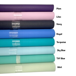 May include: A stack of colorful rolls of fabric in shades of plum, lilac, navy, royal, turquoise, sky blue, tiff blue, and mint. Each roll is labeled with its color name. The fabric has a textured surface.