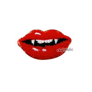 May include: A red, textured lips patch with sharp white fangs and a black mouth. The patch has the text "CraftyRific" in the lower right corner. The lips are a bold, eye-catching design.