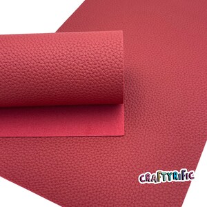 May include: A sheet of red faux leather with a textured surface. The leather is rolled up and the edges are visible. The text "CRAFTYRIFIC" is printed in white on the bottom right corner of the sheet.