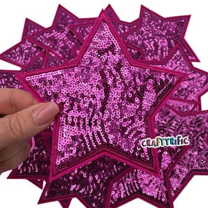 May include: A pack of ten pink sequin star iron-on patches. The stars are approximately 3 inches in diameter and have a pink felt backing. The patches are perfect for adding a touch of sparkle to clothing, bags, or other crafts. Craftyrific.