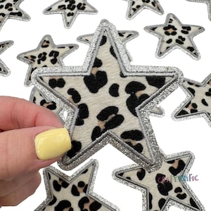 May include: A pack of 10 silver glitter star-shaped iron-on patches with a leopard print design. The patches are approximately 3 inches in diameter.
