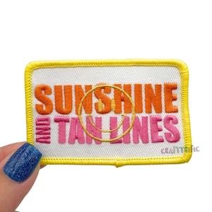 May include: Embroidered patch with the words "SUNSHINE TAN LINES" in orange and pink, with a yellow smiley face and border. The patch is rectangular and has a white background.