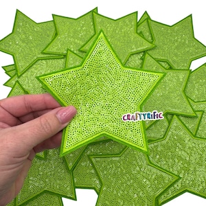 Op de afbeelding: Een stapel limoengroene stervormige patches met een glinsterende afwerking. De patches zijn ongeveer 7,5 cm in diameter. De tekst "CRAFTYRIFIC" is zichtbaar op een van de patches.