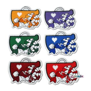 May include: Six embroidered iron-on patches in different colors. Each patch features a white heart, a white bow, and a white pom-pom. The patches are in orange, purple, green, blue, red, and white.