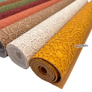 May include: A collection of rolled faux leather fabric with a lace pattern in various colors, including beige, white, orange, and yellow. The fabric is rolled up and the ends are visible. The fabric is textured and has a lace-like design.