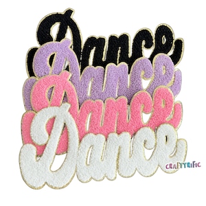May include: Four layered felt "Dance" words in black, purple, pink, and white with gold glitter trim. The words are stacked on top of each other.