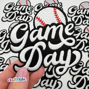 May include: White embroidered patch with the words "Game Day" in a black and white script font. A white baseball with red stitching is above the words.