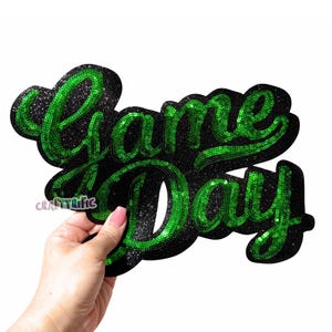 May include: Green and black sequined iron-on patch with the text "Game Day" in a cursive font.