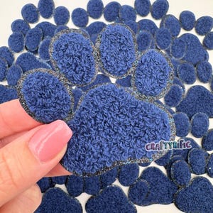 May include: A close-up of a blue paw print made of fuzzy fabric with a silver glitter trim. The paw print is surrounded by many other smaller blue paw prints.