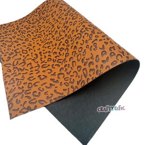 K&ouml;nnte beinhalten: Ein Blatt braunes Kunstleder mit einem gepr&auml;gten Leopardenmuster. Das Leder ist &uuml;ber einen schwarzen Untergrund gefaltet.