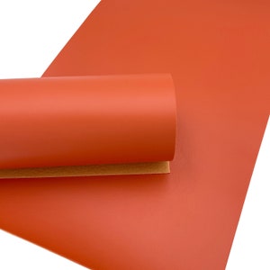 May include: A roll of bright orange faux leather. The leather is smooth and has a slight sheen.