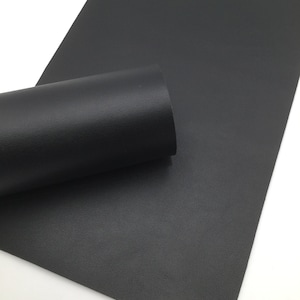 May include: A sheet of black faux leather with a textured surface. The leather is rolled up, showing the texture.