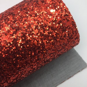 Op de afbeelding: Een rol rode glitterstof met een textuur. De stof is gevoerd met een grijs materiaal.