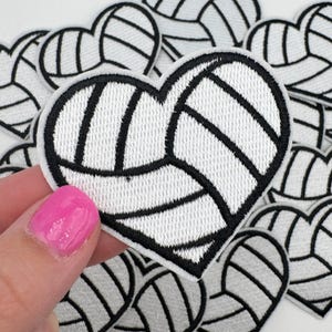 May include: Heart-shaped patch with a volleyball design. The patch features a white background with black lines and a black border. Several similar patches are visible in the background.