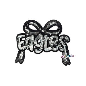 May include: A black sequined patch in the shape of a bow with the word "Eagles" in silver sequins. The patch has a white background and the text "CraftyRific" is in the lower right corner.