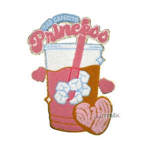 May include: A pink and brown felt patch with a cartoon image of a pink iced coffee drink with a straw and ice cubes. The text "ICED CAFEICITO PRINCESS" is above the drink. The text "CRAFTYTRIFIC" is below the drink.