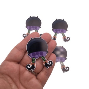May include: Five black cauldron shaped Halloween ornaments with purple and green witch legs and black shoes.