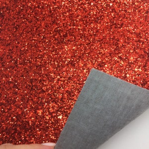 Op de afbeelding: Rood glitterstof met een grijze achterkant. De stof wordt vastgehouden door een hand.