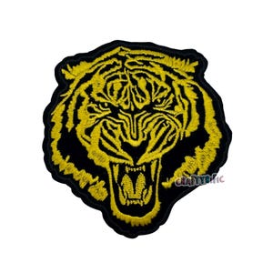 May include: Embroidered patch featuring a roaring tiger's head. The design uses yellow thread on a black background, showcasing the tiger's face with open jaws and detailed features. The patch is likely for clothing or accessories.