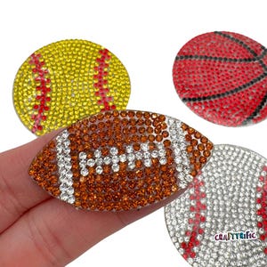 May include: Four different sports-themed iron-on patches with rhinestones. The patches are shaped like a baseball, basketball, football, and softball. The patches are all decorated with clear and colored rhinestones.