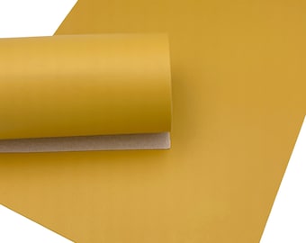 May include: Mustard yellow faux leather sheet, partially rolled, with a smooth, matte finish. The sheet is shown against a white background, highlighting the color and texture of the material. The rolled portion reveals a tan backing.