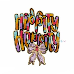May include: A colorful embroidered patch with the text "Hippity Hoppity" in a rainbow of colors. A pink and gold sequined bow is attached to the bottom of the patch.