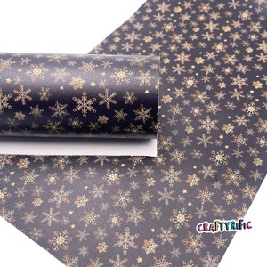 May include: Black faux leather with a gold snowflake pattern. The snowflakes are outlined in a darker gold color. The fabric is rolled up and the text "CRAFTYRIFIC" is visible in the bottom right corner.