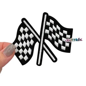 May include: Black and white checkered racing flags crossed over each other. The flags are embroidered and have a black outline.