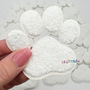 May include: White felt paw print embellishments. The paw prints are fuzzy and have a sparkly edge. The paw prints are arranged in a pile.