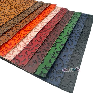 K&ouml;nnte beinhalten: Eine Sammlung von zehn Kunstlederb&ouml;gen in verschiedenen Farben mit einem gepr&auml;gten Leopardenmuster. Die Farben umfassen Braun, Orange, Rosa, Rot, Burgunder, Dunkelgr&uuml;n und Marineblau.