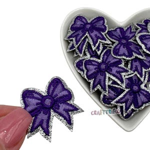 May include: A pile of purple bows with silver glitter trim. The bows are in a heart-shaped dish. The word "CRAFTYRIFIC" is visible in the bottom right corner of the image.