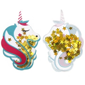 May include: Two unicorn-shaped glitter ornaments with gold glitter stars inside. The unicorns are white with pink and blue accents.