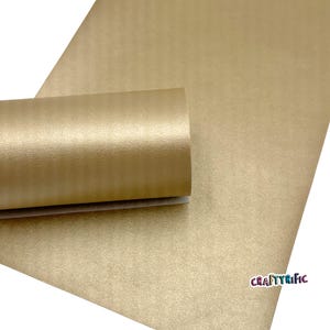 May include: A roll of gold-colored faux leather material with a textured surface. The material is partially unrolled, revealing a smooth, light-colored backing. The CraftyRific logo is visible in the bottom right corner.