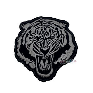 May include: Embroidered patch featuring a roaring tiger's head. The design showcases a detailed tiger face with open mouth and visible teeth, in shades of gray and black. The patch has a black border and the text "CRAFTYrific".