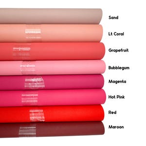 May include: A stack of fabric rolls in various shades of pink, red, and brown. Colors include sand, Lt Coral, Grapefruit, Bubblegum, Magenta, Hot Pink, Red, and Maroon. Each roll is labeled with its color name.