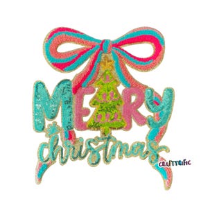 May include: A sequined Christmas decoration with the words "MERRY CHRISTMAS" in turquoise and pink. A green Christmas tree is in the center, with a pink and turquoise bow at the top. The decoration has a gold border.