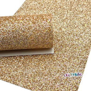 May include: A sheet of gold glitter fabric with a rolled edge. The glitter is densely packed, creating a sparkling effect. The CraftyRific logo is visible in the bottom right corner. This material is suitable for crafts and DIY projects.