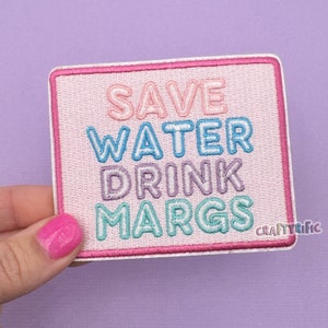 May include: Pink embroidered iron-on patch with the text "Save Water Drink Margs" in rainbow colors.